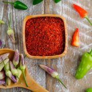 Peppers with red pepper flakes in a wooden spoon on wooden background, flat lay.
